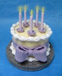 knitted birthday cake and candles with yellow cake, white frosting, light purple candles, and a purple ribbon tied around the cake